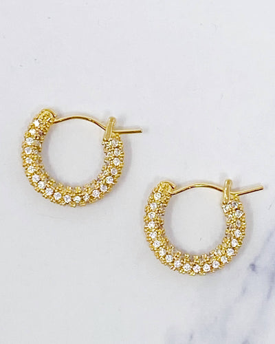The Elegant Shine Hoop Earrings are small gold hoops adorned with rows of sparkling Cubic Zirconia, beautifully displayed on a white marble surface for an elegant touch.