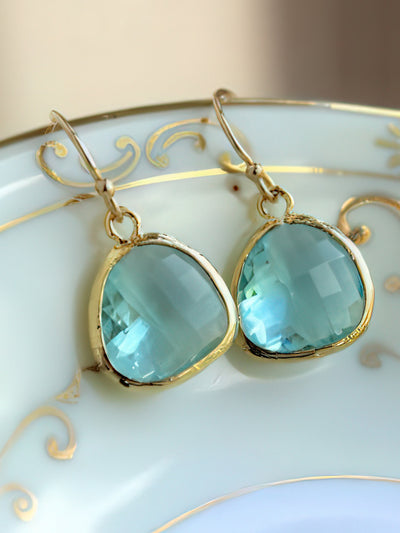 Elegant aquamarine drop earrings featuring faceted 13mm aquamarine glass gems set in 16k gold-plated bezels with 14k gold-filled ear wires, displayed on a white and gold decorative plate.