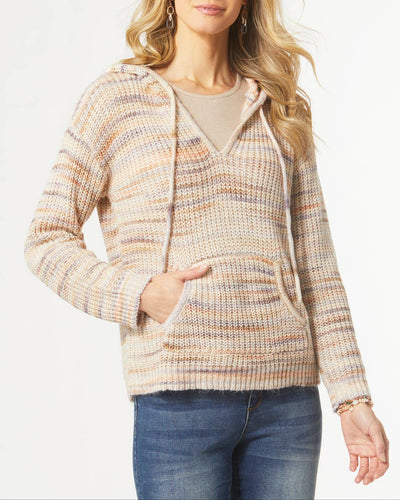 A woman wearing a cozy knit hoodie sweater in soft fall tones. The sweater features a v-neckline, attached hood with drawstrings, long sleeves, and a front pouch pocket. It has a relaxed fit and a textured knit pattern, styled with blue jeans and subtle accessories.