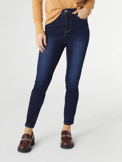 Model wearing dark Everstretch High Rise Skinny Ankle Jeans with a fitted waist, paired with a light tan top. The jeans feature a clean, streamlined silhouette with front pockets and button closure.