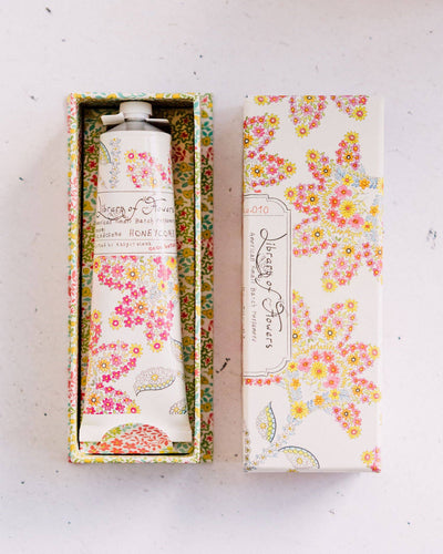 A beautifully packaged tube of Library of Flowers Honeycomb Handcreme resting inside a floral-patterned box with a matching lid set beside it.