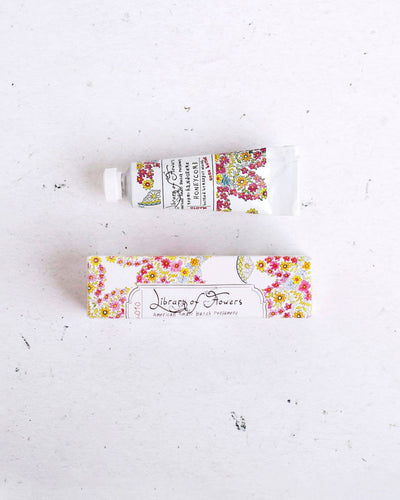 A tube of Library of Flowers Honeycomb Petite Treat Handcreme placed above its matching floral-patterned box, featuring intricate botanical designs and vintage-inspired branding.