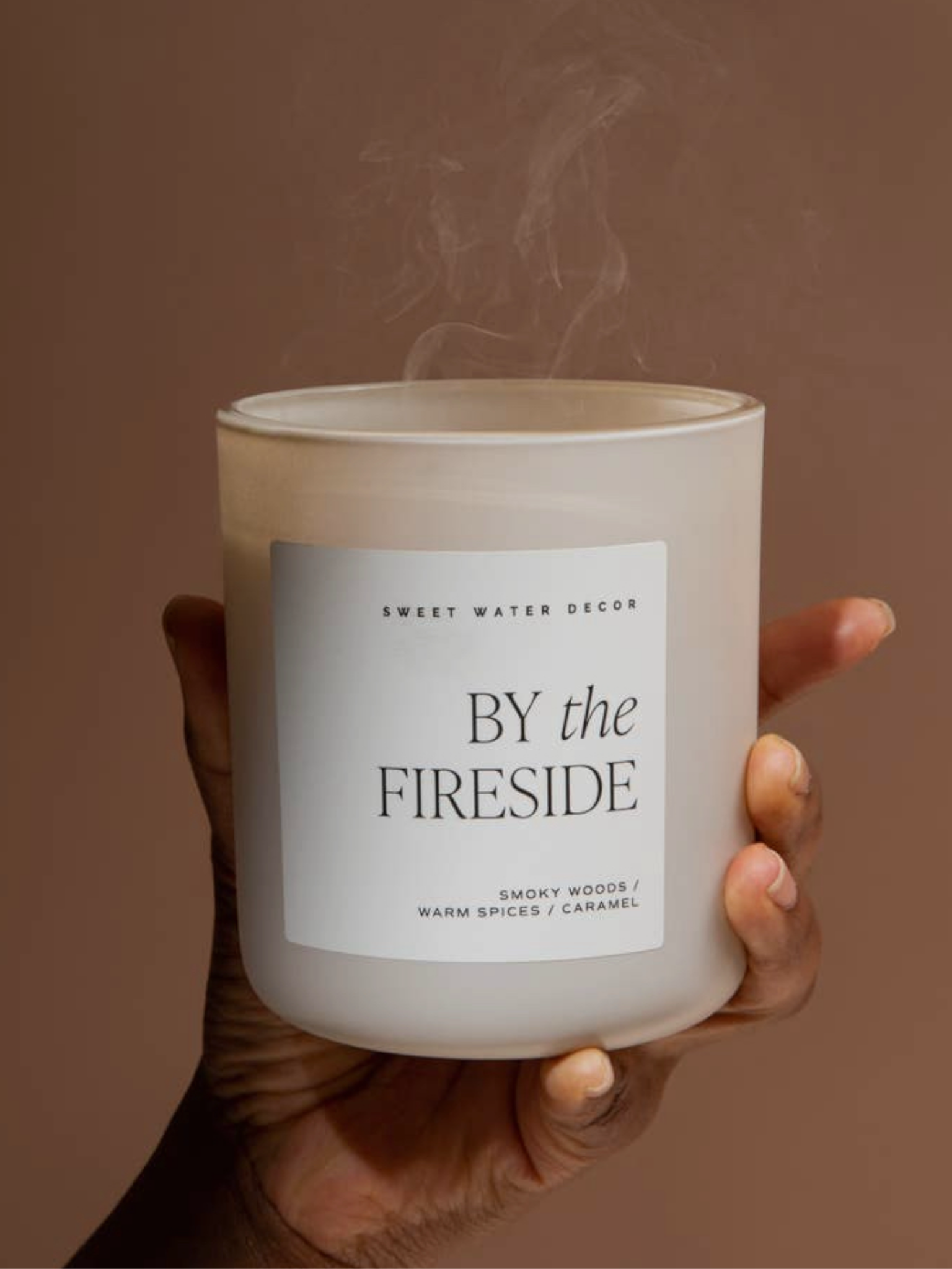 In the image, a hand holds a white candle from the Matte Jar Candle collection, named 