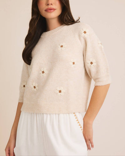 Woman wearing an oatmeal-colored short-sleeve sweater top with delicate embroidered flowers, styled with a white skirt for a soft, feminine look