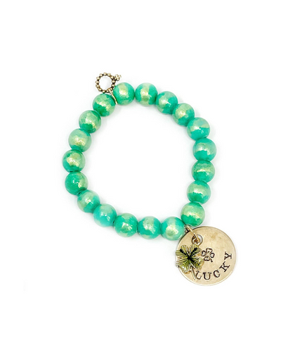 The Powerbeads by Jen bracelet features round turquoise beads, a gold-toned clasp, and a charm embossed with a leaf and the word "LUCKY." This piece resembles an Angel Kiss Agate bracelet, ideal for those who value unique accessories.