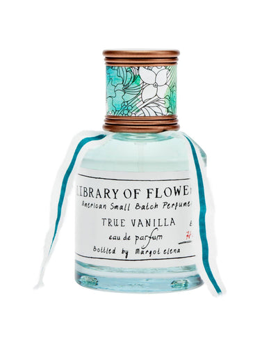 A bottle of Library of Flowers True Vanilla Eau de Parfum, featuring a clear glass design with a bronze cap wrapped in a blue and white floral pattern, a soft blue ribbon, and a handwritten-style label.