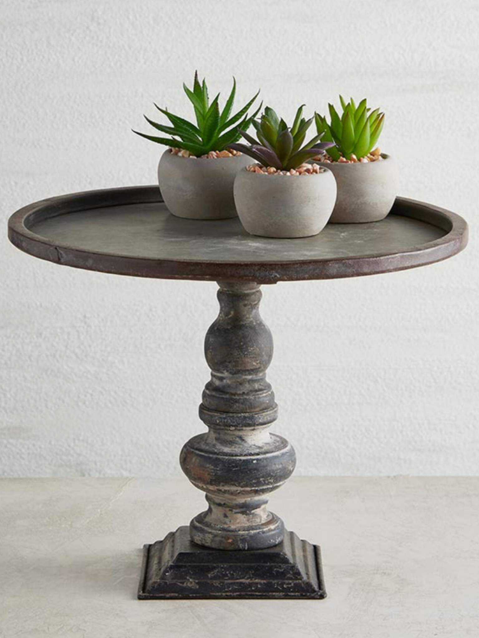 Rustic Metal Riser Stand featuring an antiqued pedestal design, displayed with small succulent planters on its 11.25-inch diameter surface, perfect for farmhouse or shabby chic décor.